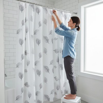 Rideau de douche blanc avec feuilles grises apaisantes avec une femme debout sur petit banc blanc