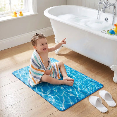 enfant avec serviette sur les épaules est assis sur le grand tapis de bain