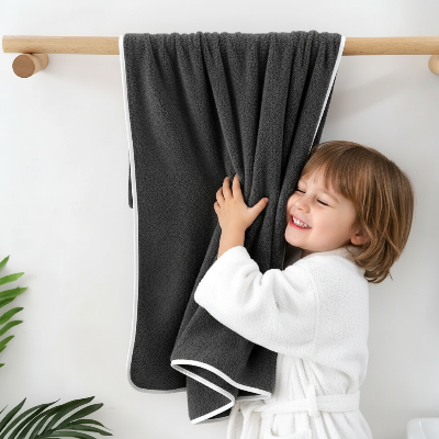 enfant qui caresse la serviette de bain en lot grise accroché sur la barre a serviettes