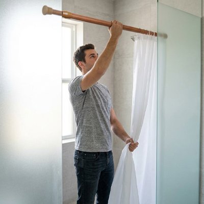 homme ajuste la barre de douche avec ses rideaux de douche
