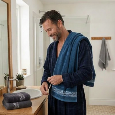 homme en peignoir avec drap de bain bleu sur son épaule avec 2 serviettes sur le comptoir et une serviette accrochée sur le crochet