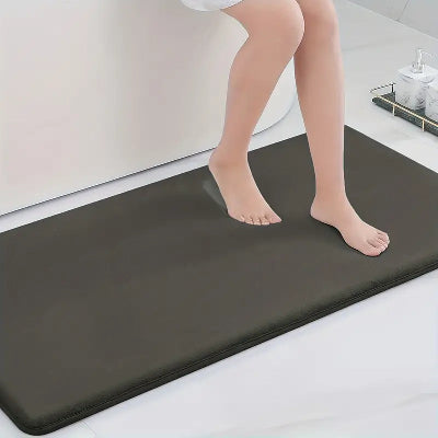 personne assise sur le rebord de la baignoire avec les deux pieds sur le tapis de bain diatomite noir 