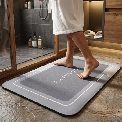 tapis antidérapant salle de bain avec inscription bathroom sur ce dernier et une personne qui entre dans la douche