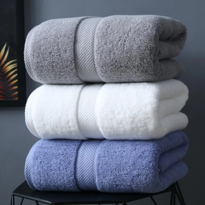 une pile de trois draps de bain bleu blanc et gris sur un petit tabouret